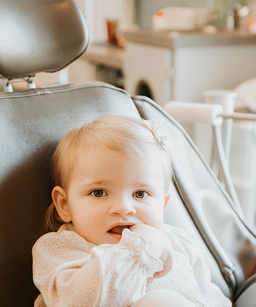 A baby sitting in the dentist's chair while chewing on a finger