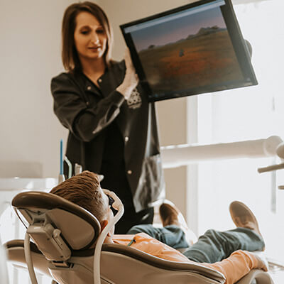 A young patient sitting in the dentist chair as an assistant adjusts the monitor